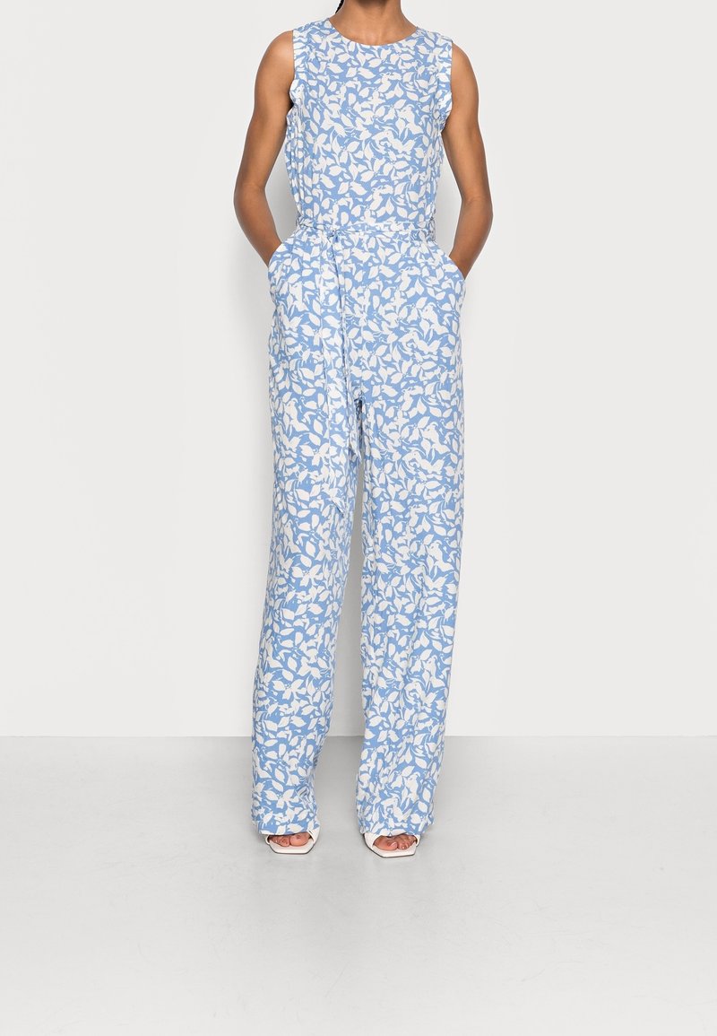 Combinaison à motifs bleu et blanc avec un design sans manches, jambes droites et poches latérales. Tissu lisse avec un motif floral.