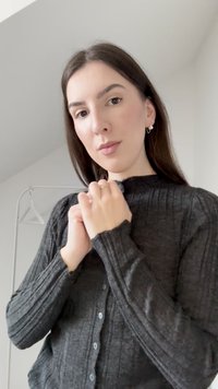 Temno siva rebrasta jopica z dolgimi rokavi in visokim ovratnikom. Ima gumbe spredaj in teksturirano tkanino za dodaten detajl.