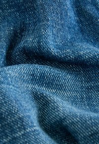 Denim w głębokim niebieskim kolorze o teksturowanym splocie, z delikatnymi różnicami w odcieniu i miękkim wykończeniu, układający się w łagodne fałdy.