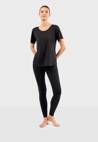 Top noir à manches courtes avec un col rond associé à un legging noir avec des panneaux en mesh sur les côtés, tous deux fabriqués dans un tissu doux et extensible.