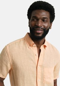 Kurzärmliges Button-Down-Hemd aus leichtem Pfirsichleinen mit einer Taschenanordnung auf der linken Seite und einem strukturierten Stoff für Atmungsaktivität.