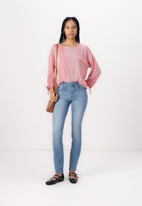 Top de manga larga a rayas rojas con cordones, jeans ajustados de color azul claro y bailarias negras, complementados con un pequeño bolso cruzado marrón.
