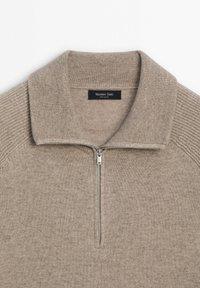 Pull taupe en maille avec demi-fermeture éclair, col et épaules côtelés, doté d'une fermeture éclair argentée et d'une étiquette de marque à l'intérieur du col.