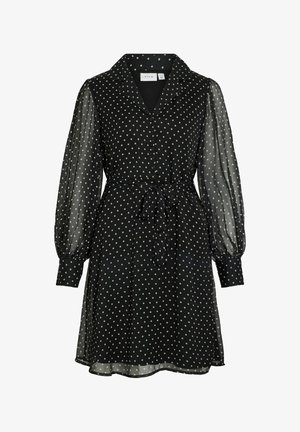 Zwarte jurk met witte polka dots, voorzien van een kraag, lange doorschijnende pofmouwen, een ceintuur in de taille en een vloeiende zoom.