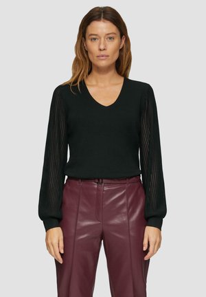 Zwarte gebreide trui met een v-hals en gestreepte doorschijnende lange mouwen, gecombineerd met hooggewaagde bordeaux leren broek.