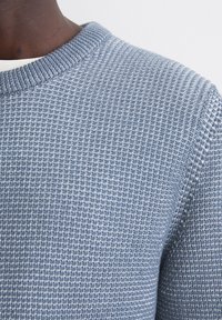 Texturiertes blaues Strickpullover mit einem gerippten Rundhalsausschnitt, der ein gewebtes Muster und glatte, weiche Stoffdetails hervorhebt.