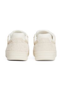 Zapatillas blancas con un trasero texturizado en color crema, parte delantera lisa, cuello acolchado y suelas de goma ligeras. Diseño minimalista sin marcas visibles.