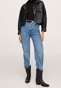 Veste en cuir noire courte portée sur un col roulé noir, associée à un jean taille haute bleu clair et des bottes de cowboy noires.