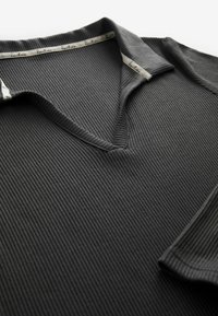Polo shirt gris foncé à côtes avec un col en V. Présente un tissu texturé et un design subtil sans embellissements supplémentaires.