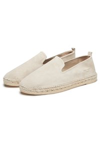 Chaussures à enfiler en suède beige avec des semelles en style espadrille tissées, bout arrondi et branding subtil sur le côté. Texture douce et design simple.