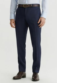 Granatowe spodnie dopasowane, z delikatnym wzorem w kratk�ę, teksturą materiału oraz brązowym skórzanym paskiem. Całość uzupełniają brązowe buty eleganckie.
