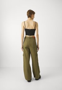 Zwarte cropped top met dunne bandjes en een rits aan de achterkant, gecombineerd met olijfgroene wijde cargobroek met zakken en een bruine tailleaccent.