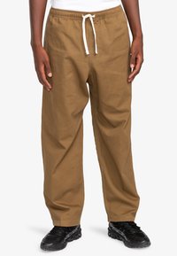 Bruine, loszittende broek met een elastische tailleband en koord. Gemaakt van textuurstof, met zijzakken en rechte pijpen.