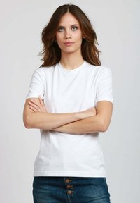 T-shirt bianco in cotone con maniche corte e scollo rotondo, indossato con jeans in denim blu con dettagli in bottone di ottone.
