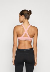 Rosa sportbh med korsad ryggdesign och logodetalj. Kombinerad med svarta tajta leggings med en märkesmidja. Slät textur.