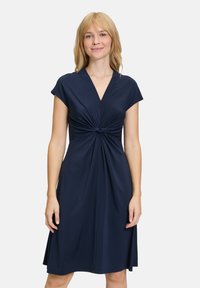Robe bleu marine avec un décolleté en V et des manches courtes, dotée d'un détail de nœud torsadé à la taille et d'une jupe fluide. Texture de tissu lisse.