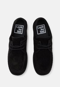 Chaussures en daim noir avec des détails en dentelle, présentant un bout arrondi et des bords cousus. Les semelles intérieures affichent une étiquette "Levi's for feet".
