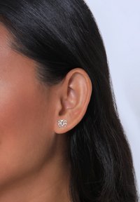 Boucles d'oreilles puces en argent sterling en forme de fleur de lotus avec un délicat motif découpé. Présentées sur l'oreille d'un modèle avec des cheveux noirs lisses.