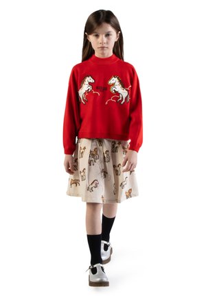Rode gebreide trui met paardenmotieven en "KENZO" logo, gecombineerd met een beige rok met speelse paardenpatronen. Zwarte sokken en zilveren schoenen.