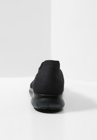 Chaussure de sport noire avec une tige en tissu texturé et une semelle en caoutchouc flexible, conçue pour le confort et la facilité de mouvement, vue de derrière.