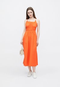 Oranžové šaty bez rukávov s žabičkovaným živôtikom, voľným midi strihom a ľahkou látkou. Doplněné bielymi teniskami a malou kabelkou.