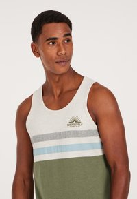 Lightweight tank top in beige with horizontal stripes in gray, light blue, and olive green. Features logo print and a crew neckline.
