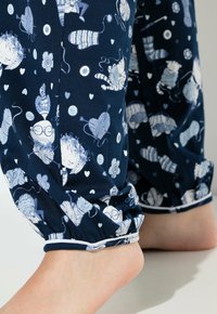Pantalones de pijama azul marino con un patrón juguetón blanco de gatos, ovillos de lana y flores; puños elásticos con un ribete en contraste en los tobillos.