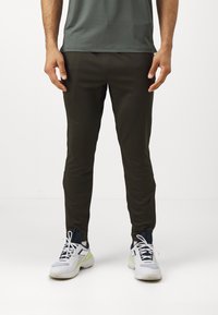 Dunkelgrüne Sporthose mit schmaler Passform, glatter Textur und elastischem Bund, kombiniert mit weißen und grauen Sneakers.