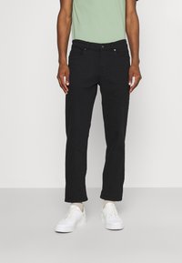 Jeans de mezclilla negra con un diseño de pierna recta, estilo de cinco bolsillos y una textura sutil. Combinados con zapatillas blancas y una camiseta de color verde claro.