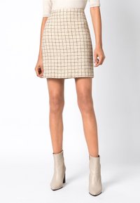 Mini gonna in tweed beige con un motivo a quadri neri. Il tessuto ha una finitura testurizzata. Abbinata a stivaletti beige chiaro con un design elegante.
