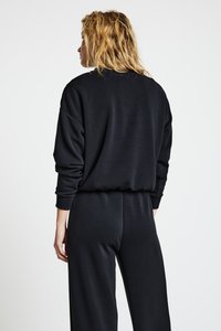Sweat-shirt noir à manches longues avec une coupe ample. Il présente des poignets et un ourlet côtelés, confectionné dans un tissu doux et texturé.