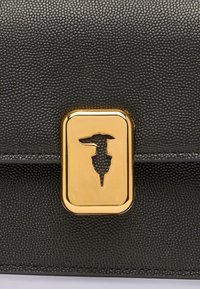 Borsa in pelle nera testurizzata con una chiusura rettangolare dorata che presenta un contorno ritagliato di una donna che indossa un cappello.