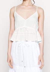 Top peplum azzurro chiaro con spalline sottili, scollatura a V, vita arricciata e dettagli in pizzo. Realizzato in un tessuto leggero e testurizzato.