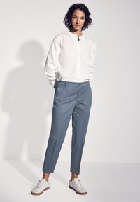 Biała koszula z długim rękawem, z zapięciem na guziki i falbaniastego kołnierza, zestawiona z jasnoniebieskimi dopasowanymi spodniami i białymi trampkami z brązowymi podeszwami.