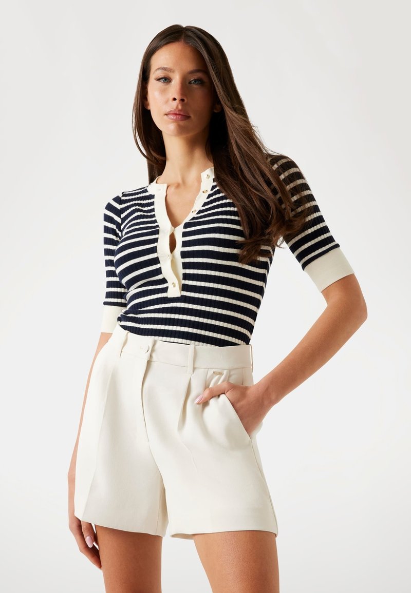 Navy and white striped ribbed top with short sleeves and button placket, paired with cream high-waisted pleated shorts. Soft texture.