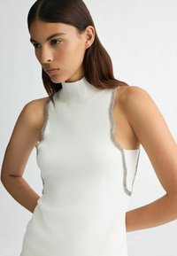 Top bianco senza maniche con un collo alto, caratterizzato da dettagli in catena argentata lungo le aperture delle maniche e un design testurizzato e aderente.