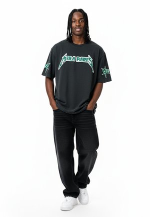 T-shirt nera a maniche corte con grafica verde "PARIGI" e design a stella. Indossata con jeans scuri e sneakers bianche. Vestibilità comoda.