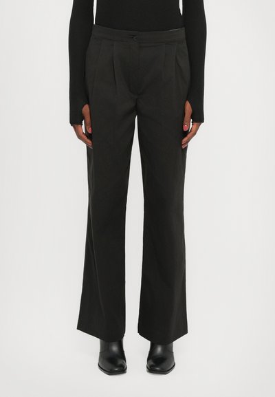 Pantalones negros de pierna ancha hechos de una tela suave, que cuentan con pliegues frontales y un cierre de botón en la cintura, combinados con botas negras hasta el tobillo.