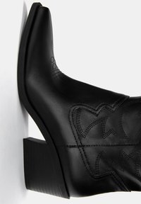 Zwarte leren cowboylaars met een spitse neus, blokhak en decoratieve stikpatronen aan de zijkant. Gladde textuur en slank ontwerp.