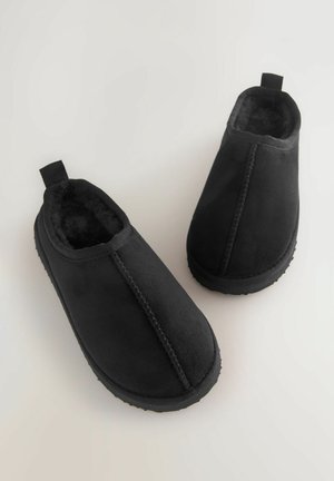 Schwarze Slipper mit einem weichen, kuscheligen Innenfutter. Das Material wirkt wie Wildleder, mit einer glatten Außenseite und Gummisohlen mit strukturiertem Grip.