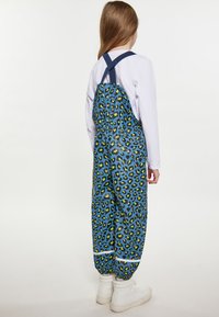 Salopette in stampa leopardata blu e verde con vestibilità rilassata, spalline regolabili e polsini elasticizzati. Realizzata in materiale lucido e liscio.