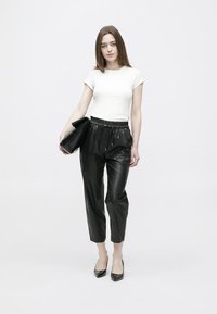 Mustad, läikivad, plisseeritud püksid elastse vöökohaga, kombineeritud istuva valge t-särgiga. Modell hoiab musta käekotti ja kannab musti kontsakingi.