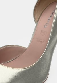 Μεταλλικό ασημί γυναικείο παπούτσι με ψηλό τακούνι, απαλής υφής, σχεδιασμένο με ανοιχτά δάχτυλα και εσωτερική επένδυση σε ροζ απόχρωση. Διακοσμημένο με διακριτικές ραφές.