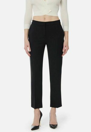 Donna che indossa pantaloni neri a gamba dritta, décolleté nere a punta e un cardigan corto bianco con bottoni.
