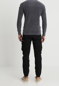 Grauer gerippter Pullover mit Rundhalsausschnitt und langen Ärmeln, kombiniert mit schwarzen Cargohosen mit Seitentaschen und elastischen Bündchen. Beige Sneaker.
