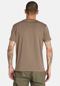 Maglietta in cotone marrone con maniche corte e collo rotondo, caratterizzata da una texture liscia e una vestibilità rilassata, indossata con pantaloni cargo color oliva.