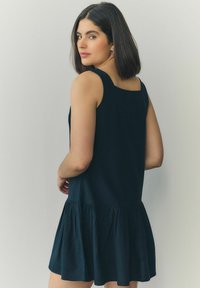 Rochie neagră fără mâneci, cu un corset ajustat și o fustă evazată. Prezintă un tiv strâns și un decolteu pătrat, fiind confecționată dintr-un material ușor.