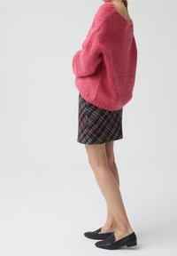 Roze gebreide oversized trui met gestructureerde strepen, gecombineerd met een meerkleurige geruite minirok en zwarte platte schoenen.
