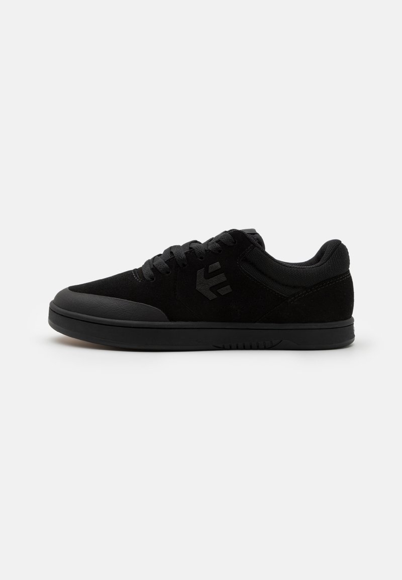 Black low-top sneaker with suede and mesh upper, black laces, rubber sole, and subtle logo on the side, shown on a white background.