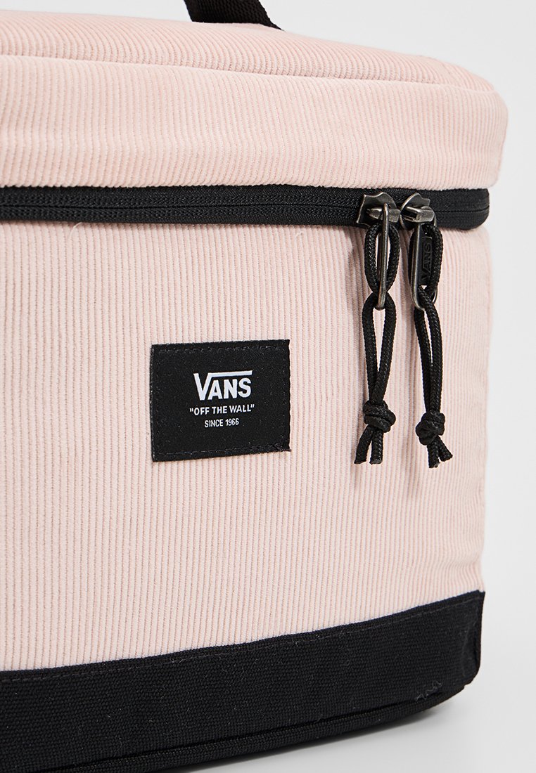 Bolso de pana rosa con base negra, cierres duales y etiqueta del logo de Vans. Presenta una tela texturizada y detalles de acento con cordón.